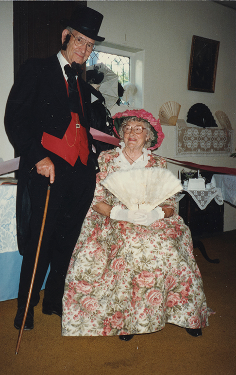 Photograph of bespectacled and smiling older white man (standing) and woman (seated) in Edwardian dress.